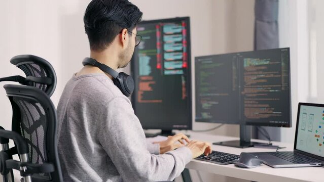 An Asian male programmer is intensely focused on coding, surrounded by multiple monitors and a tablet, showcasing a high-tech multitasking workspace.