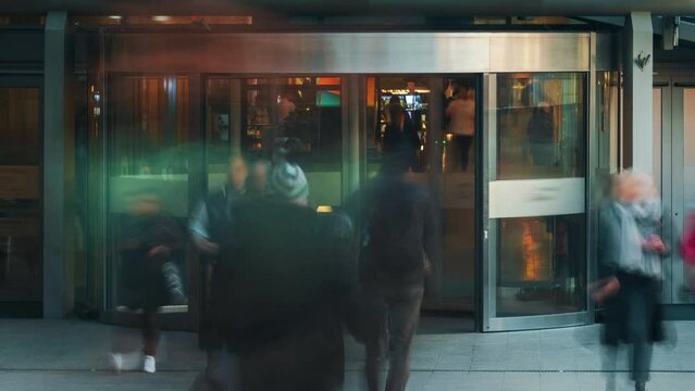 Time-lapse busy shopping mall entrance unrecognizable people crowd enter and exit store through revolving door. Rush hour crowded shopping center, glass door rotating fast motion, blurred faces