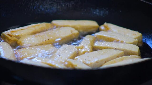 Frying tofu slices in hot oil in fry pan on kitchen stove close up