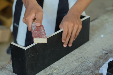 Hands of a carpenter manually sanding wooden with sandpaper in a woodworking or carpentry workshop