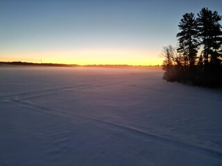 Stunning winter landscape featuring a tranquil snow-covered field illuminated by a golden sunset