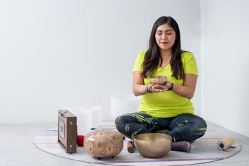 Mexican woman meditating in a yoga studio while holding a Tibetan singing bowl in her hands.