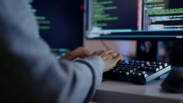 A close-up shot of a programmer's hands on a mechanical keyboard, coding late at night with focused precision on multiple screens.