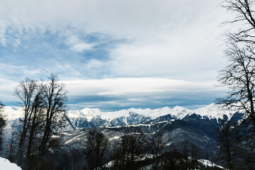 Mountain scenery to snowy peaks from the ski slope with fluffy clouds in the blue sky. Overcast. Copy space. Top view 