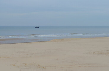 Single fishing boat on the North Sea on a calm, overcast day in spring with empty beach in front