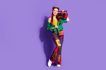 Full length photo of adorable pleasant girl wear print pants holding retro boombox on shoulder isolated on violet color background