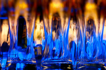 Reihe blau-orange leuchtender, gespülter Weizenbiergläser am Tresen einer Bar in schummriger Barbeluchtung mit selektiver Schärfe