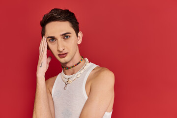 good looking gay man in casual attire with accessories on red background and looking at camera