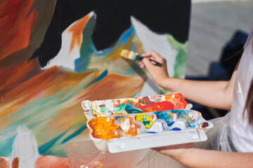 Female painter hand passionately paints picture with paintbrush for outdoor street exhibition using vibrant colors, close up view