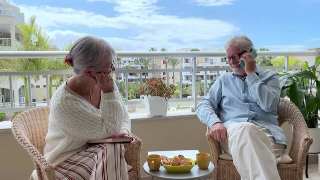Candid capture of relaxed couple of seniors enjoying lifestyle in retirement, elderly 70 years old people talking sitting outdoors on terrace