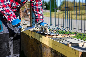 A man in overalls and gloves is repairing the fence in front of the family house. Close-up view and...