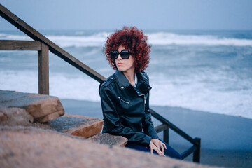 Portrait of an adult Arab woman with red curly hair in casual clothes in a beach at a rainy day