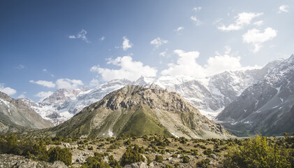 Fototapeta premium Mountain panoramic landscape of the Fan Mountains with rocks, glaciers and vegetation in sunny weather with blue sky, mountain panorama in Tajikistan in the early evening