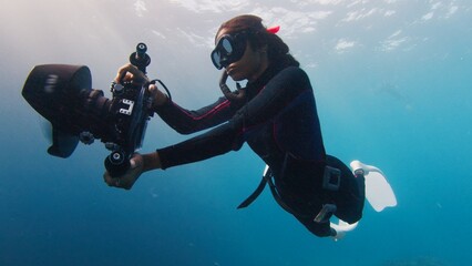 Female Indian underwater photographer swims with big underwater camera. Female freediver with...