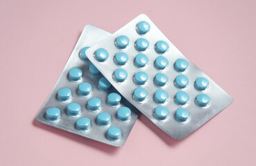 Two blisters of blue tablets on a pink background