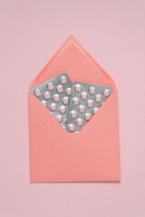 Envelope with blisters of tablets on a pink background