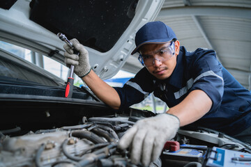 A mechanic is working on a car engine, wearing a blue shirt and a blue hat. He is wearing gloves...