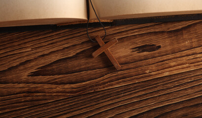 Open Bible book and wooden Christian cross on a string, wooden table