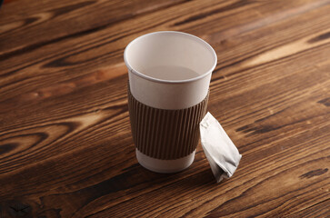 Cardboard cup for hot drinks and tea bag on wooden background