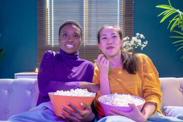 Portrait of funny and happy young women watching comedy in bed and laughing. Cheerful friends eating tasty popcorn and looking movie with gladness. Cozy and friendly atmosphere. High quality photo
