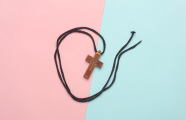 Wooden Christian cross on a string, pink blue background