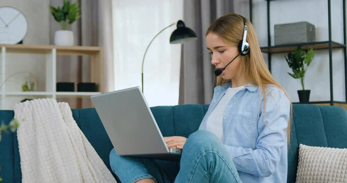 Business freelance woman in headset controlling time on smart watch during online video meeting sitting on soft couch at home