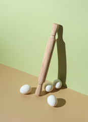 Wooden rolling pin and eggs on a colored pastel background with shadow