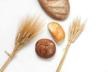 Buns and bread with ears of wheat and rye on a white background. Top view