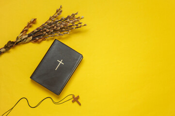 Willow twigs and Holy Bible book and cross on yellow background. Top view. Flat lay. Copy space