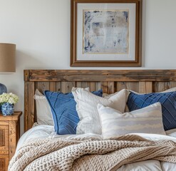 A bedroom with wooden headboard, blue and white pillows on the bed, beige blanket, wood bedside table