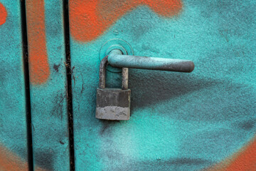 Locked padlock on doorhandle of graffiti painted metal entrance. Blue and orange colors and horizontal view.