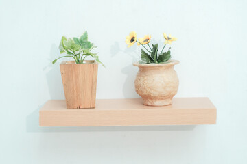 Wooden shelves with beautiful plants, alarm clock, toy cars and books on a light wall