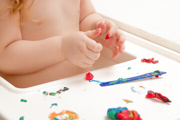 Obraz na płótnie Canvas Baby hands holding and kneading red modeling clay on white table background. Closeup. Point of view shot. Toddler development. Making different colorful shapes.