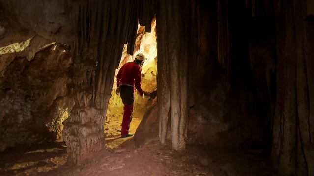 A speleologist with a headlamp exploring a cave with rich stalactite and stalagmite formations. High quality 4k footage