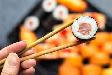 Women's hands hold sushi roll with sticks close up. Blurred dark background