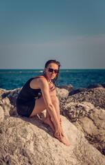 A young beautiful girl posing on a rocky sea beach in a short black dress