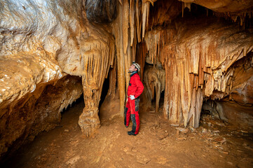 A speleologist with helmet and headlamp exploring a cave with rich stalactite and stalagmite...