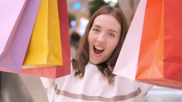 Happy young beautiful woman in shopping center mall between shops store. Delighted female lady with shopping gift packages bag on sale or discount day or black friday indoor plaza 4K