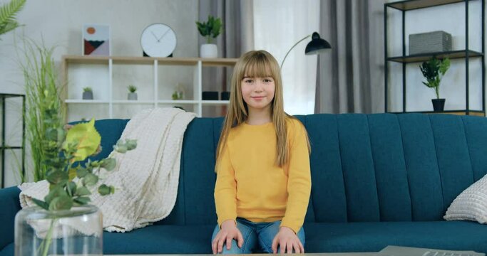 Portrait of smiling girl in casual clothes looking at camera with satisfied face sitting on soft couch in living-room
