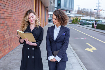 Two successful business women are talking in the city in front of a modern building. Business meeting on the street. 2 female managers with top positions.