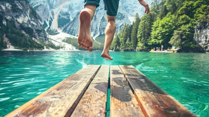  Close-up of man's feet jumping off a wooden jetty into a mountain lake © Paula