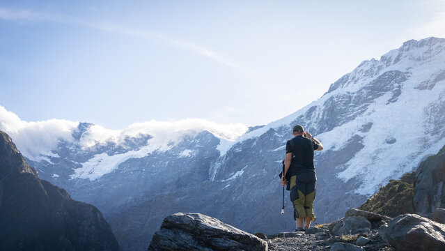 Man on lookout point taking photos of massive glaciers and mountains towering above him, New Zealand