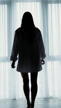 Silhouette of attractive girl in white underwear. near the window. Vertical video.