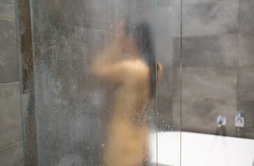 Unfocused portrait of a woman showering through the bath screen with little drops