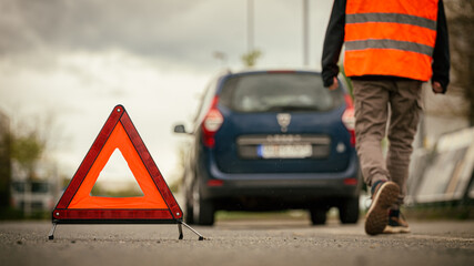 Warndreieck warnt vor Autopanne - Mann mit Warnweste im Hintergrund
