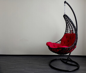 In a room with white walls, on the background of the wall there is a hanging cocoon chair made of...