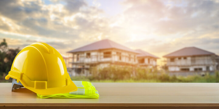 Yellow safety construction helmet on wood table with construction site background
