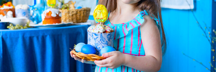 pretty little Armenian girl helps with baking for Easter on veranda on sunny spring day decorated with flowers and Easter decor, eggs, cake and willow branches, Easter family celebration