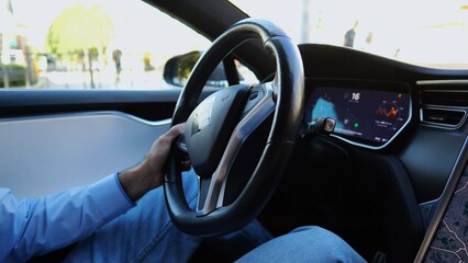 Hands of businessman holds steering wheel while driving electric car at city. Male businessperson...