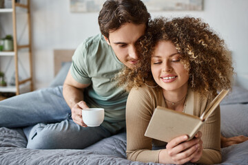 Morning cuddles and book time for curly young woman as brunette man lovingly embraces her